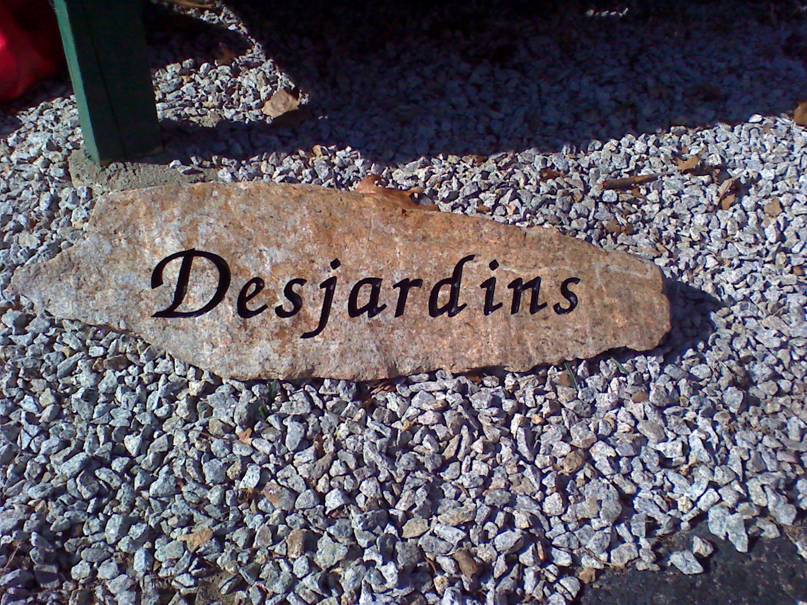 A natural fieldstone slab lettered Desjardins in black script, set into a bed of gravel