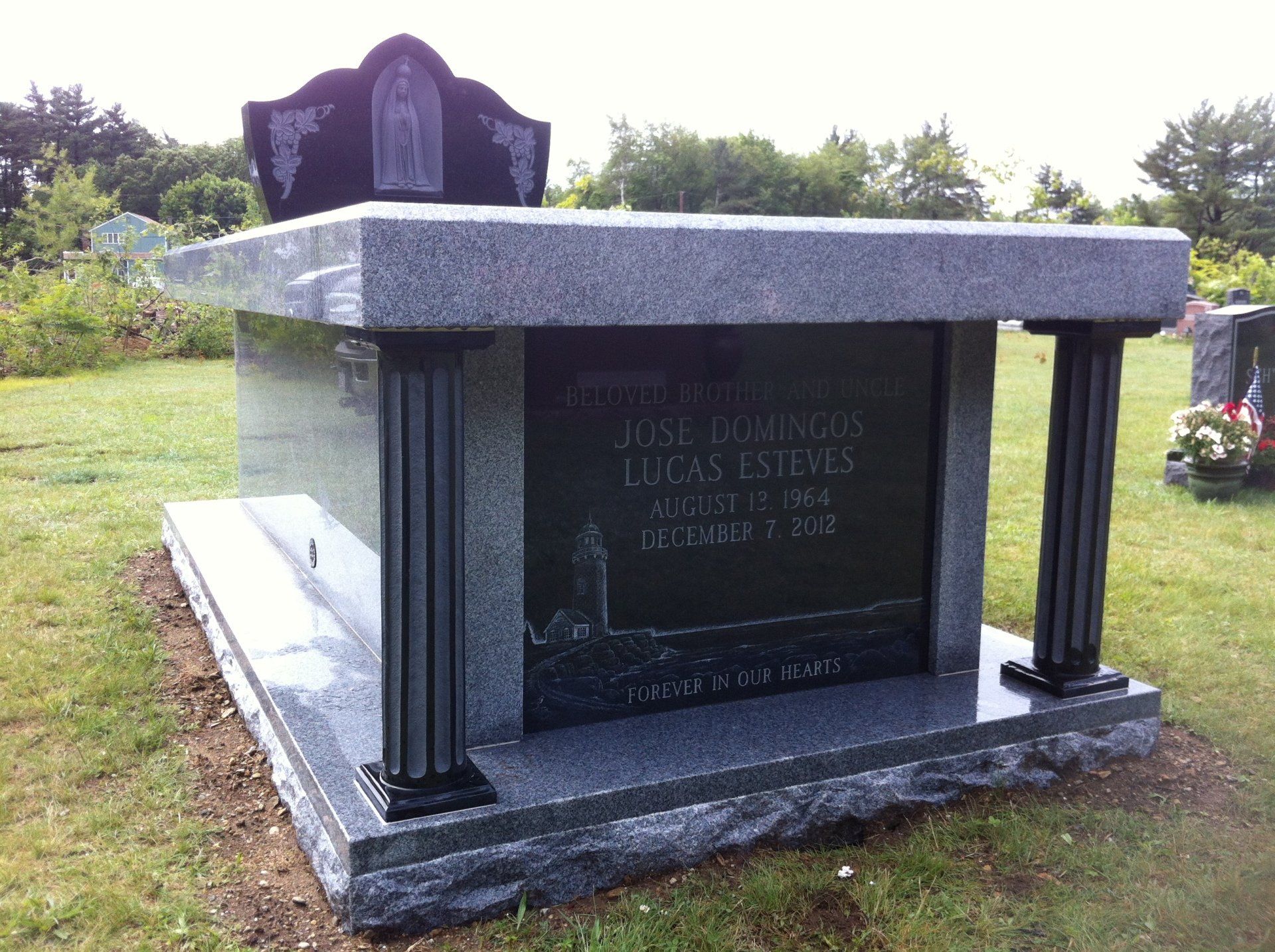 A granite walk-in mausoleum on fluted black columns, with a carved Fatima figure in the crest and a black panel etched with a lighthouse and shoreline