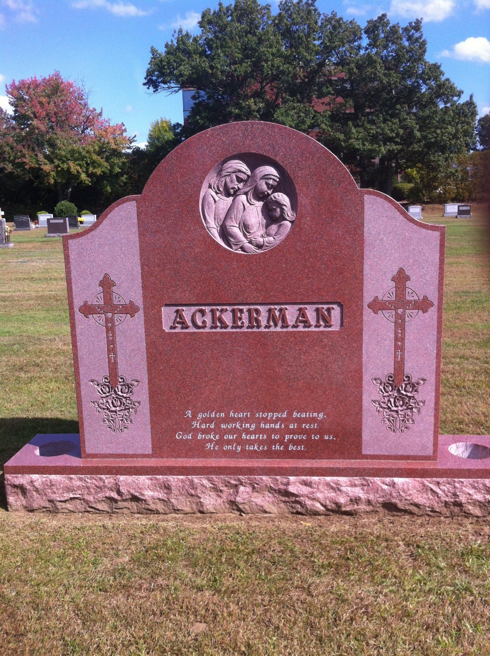 Red granite family monument lettered Ackerman, with a carved family relief in a roundel and two carved crucifix and rose panels