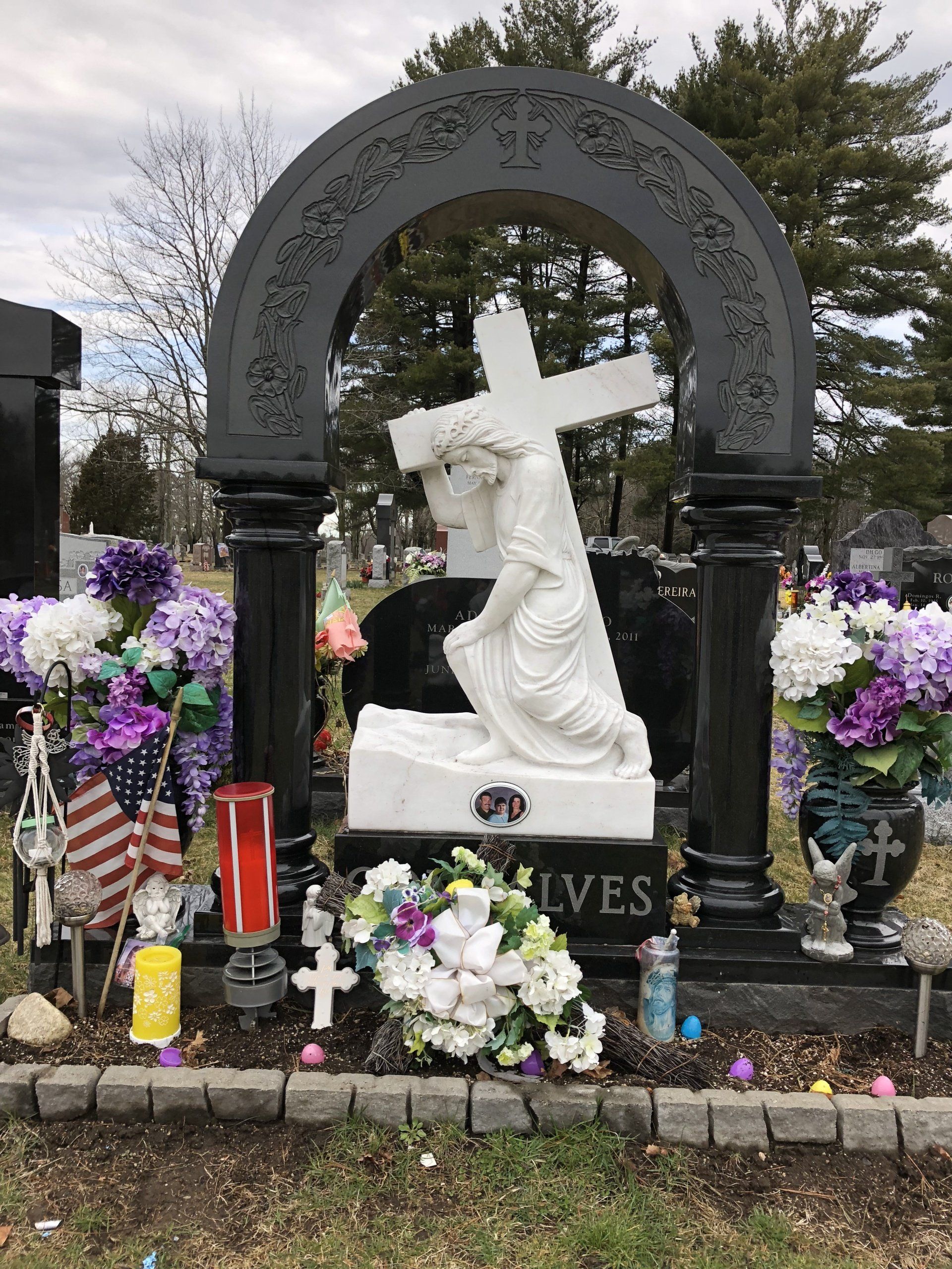 A black granite arch on two turned columns with a carved floral border and cross, sheltering a white marble figure carrying a cross