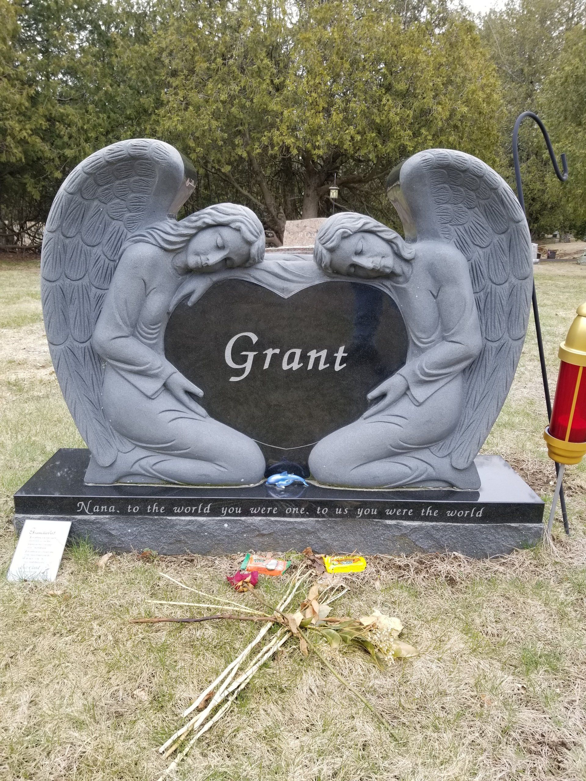 Two carved kneeling granite angels holding a polished black heart lettered Grant, standing in a cemetery