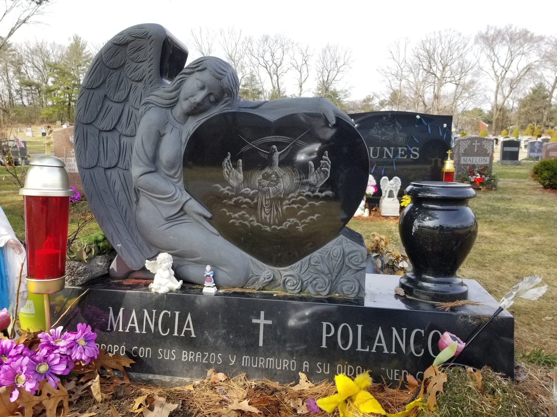 Dark granite kneeling angel embracing a polished heart etched with a religious scene, lettered Mancia and Polanco with a Spanish inscription