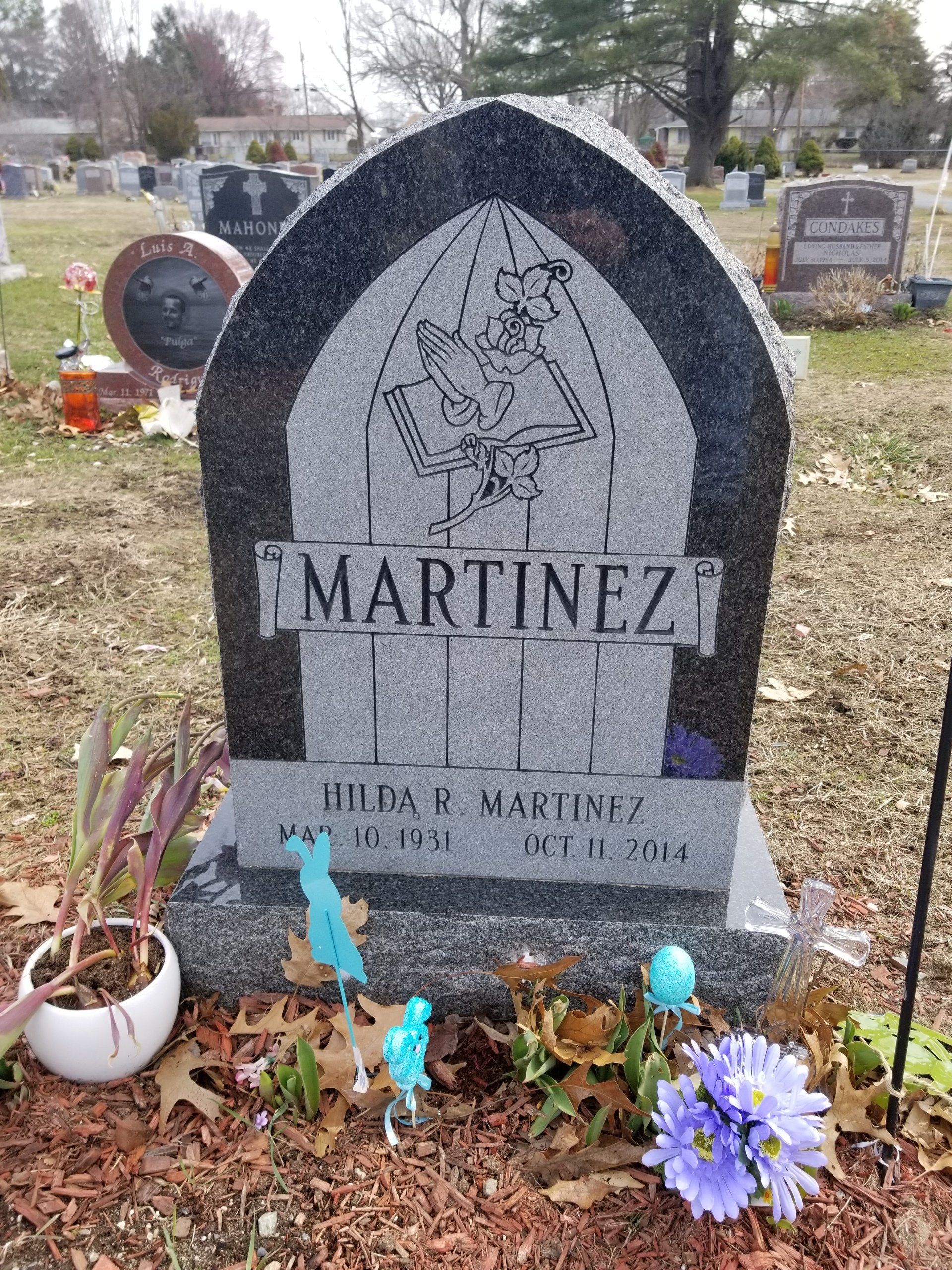 Dark granite gothic arch monument with carved praying hands over an open book and a rose, and a scroll panel lettered Martinez
