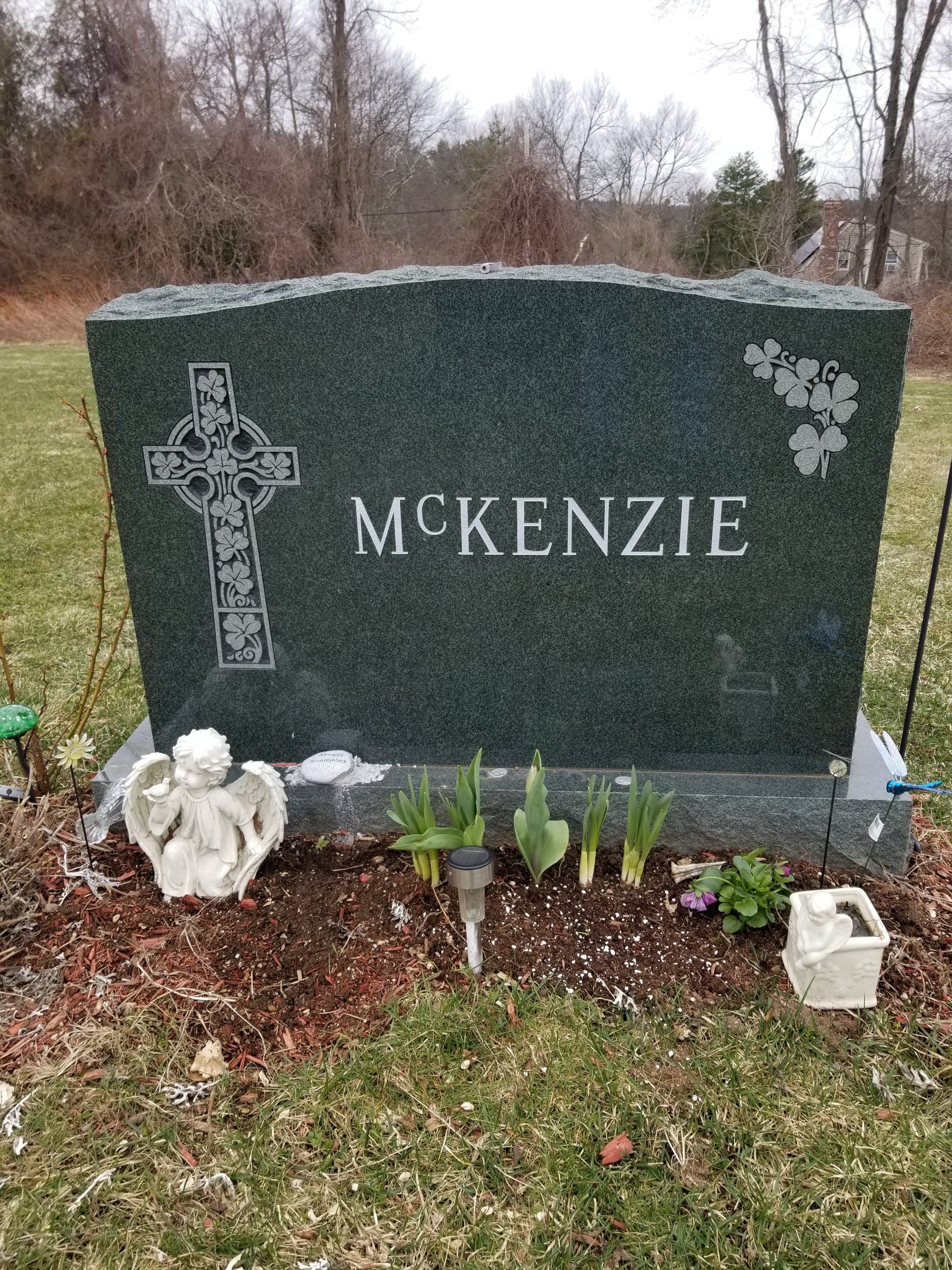 Green granite upright monument with a rough-hewn top, a carved Celtic cross filled with shamrocks and a shamrock corner spray, lettered McKenzie