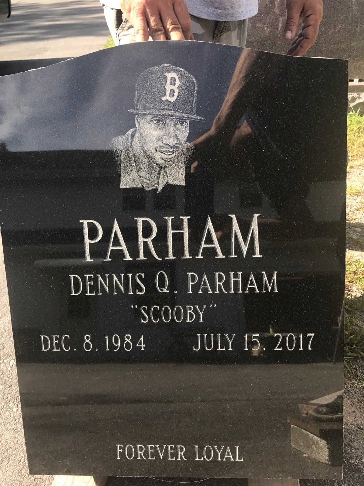 Black granite tablet held upright by hand in the shop, carrying a photographic portrait etching of a man in a Boston cap, inscribed Forever Loyal